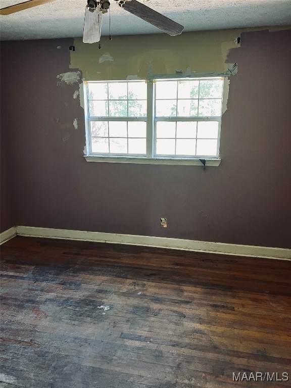 empty room with a textured ceiling, a healthy amount of sunlight, dark wood-type flooring, and ceiling fan