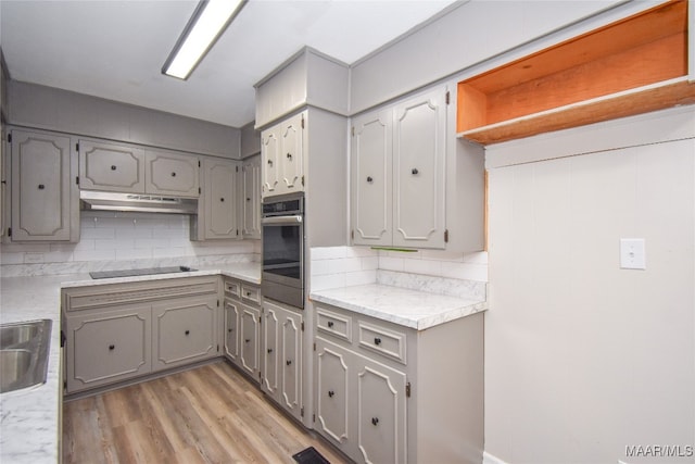 kitchen featuring backsplash, stainless steel oven, light wood-type flooring, black electric cooktop, and gray cabinetry