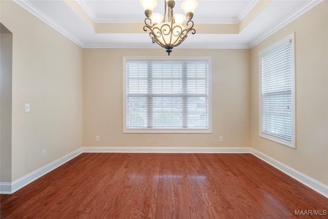 empty room with ornamental molding, hardwood / wood-style flooring, a tray ceiling, and a notable chandelier