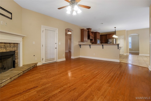 unfurnished living room featuring ceiling fan, light hardwood / wood-style flooring, and a stone fireplace