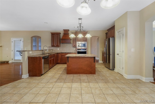 kitchen featuring kitchen peninsula, stainless steel appliances, custom range hood, pendant lighting, and sink