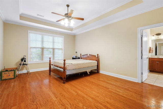 bedroom featuring ceiling fan, light hardwood / wood-style floors, ensuite bath, a tray ceiling, and ornamental molding