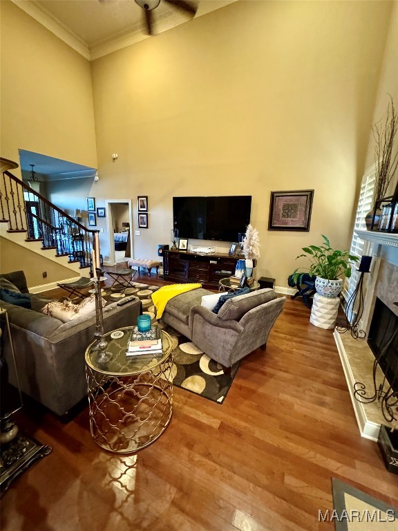 living room featuring a towering ceiling, a high end fireplace, hardwood / wood-style flooring, and ornamental molding