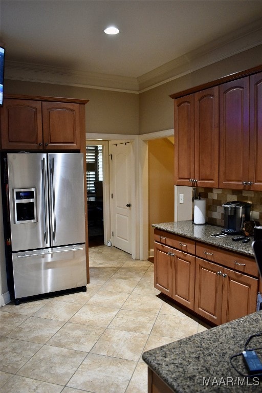 kitchen featuring light tile patterned flooring, stainless steel fridge, dark stone counters, crown molding, and decorative backsplash