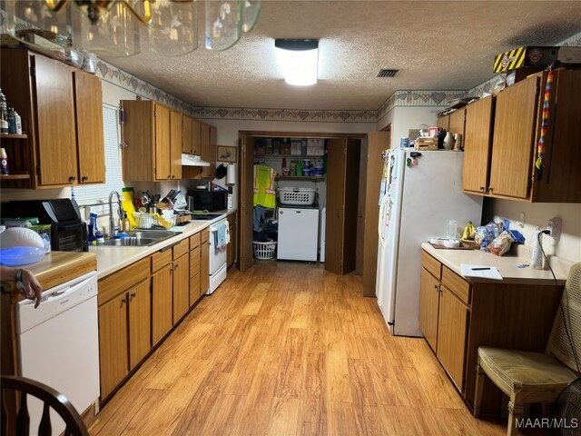 kitchen with a textured ceiling, sink, light wood-type flooring, washer / clothes dryer, and white appliances