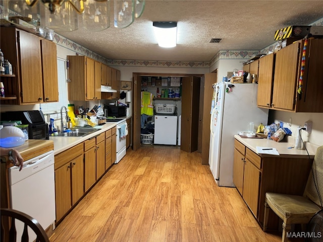 kitchen with washer / dryer, white appliances, light countertops, under cabinet range hood, and a sink