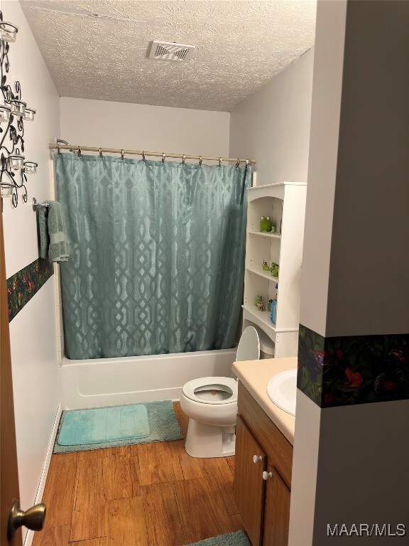 full bathroom with a textured ceiling, wood-type flooring, vanity, shower / bath combo, and toilet