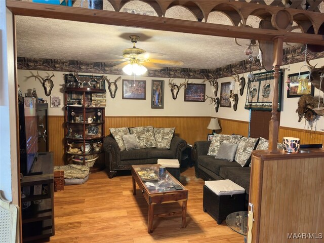 living room featuring hardwood / wood-style floors, wooden walls, a textured ceiling, and ceiling fan