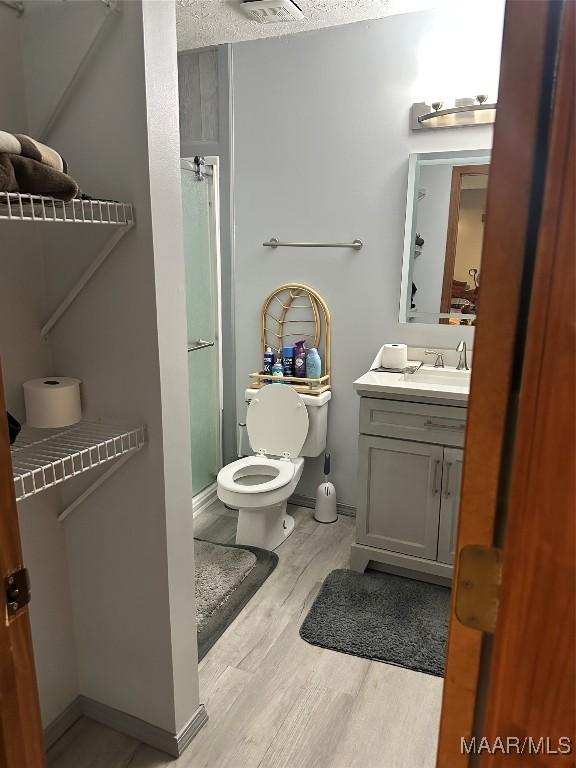 bathroom with vanity, wood finished floors, toilet, baseboards, and a stall shower