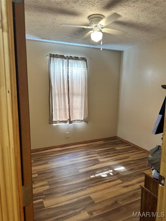 empty room with ceiling fan, a textured ceiling, and wood finished floors