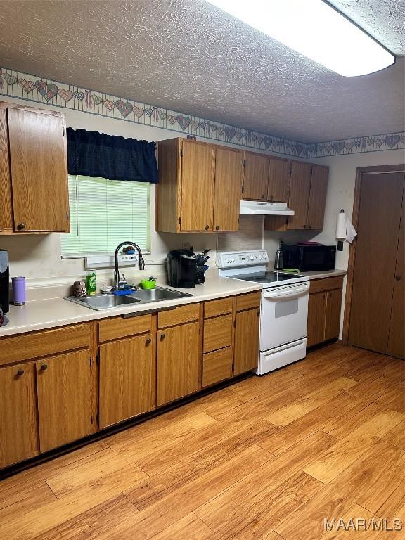 kitchen with light wood-style floors, a textured ceiling, under cabinet range hood, a sink, and white electric stove
