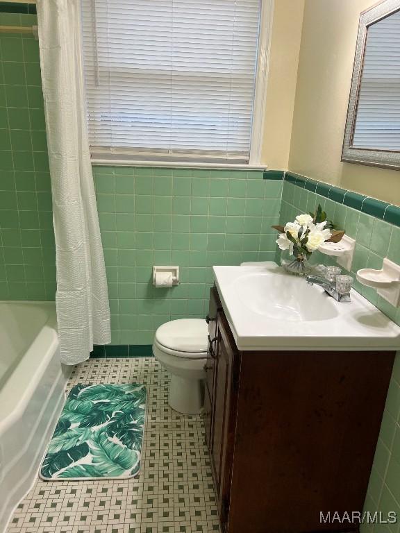 full bathroom featuring vanity, shower / bath combination with curtain, toilet, and tile walls