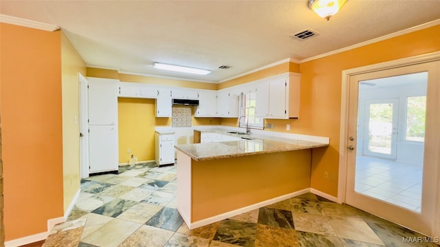 kitchen featuring light stone counters, kitchen peninsula, sink, ornamental molding, and white cabinetry