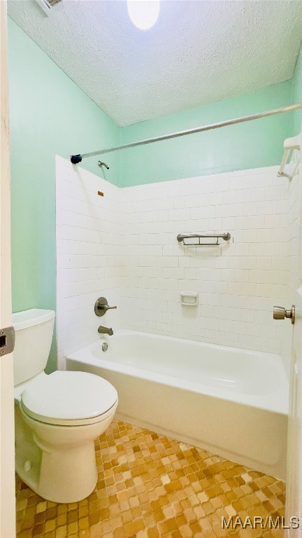 bathroom featuring a textured ceiling, toilet, and tiled shower / bath