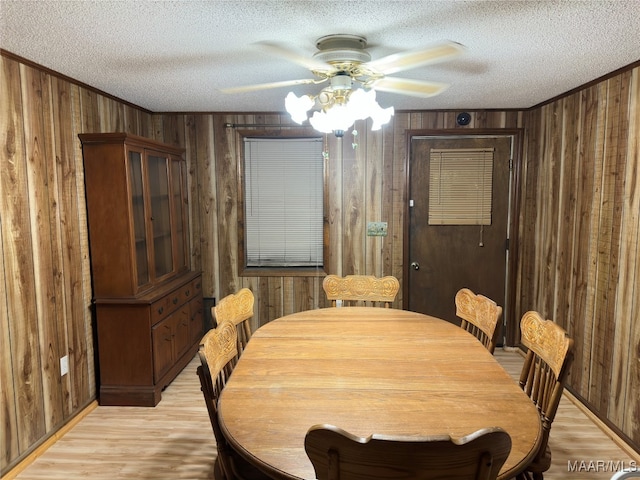 dining room with wooden walls, a textured ceiling, ceiling fan, and light hardwood / wood-style flooring