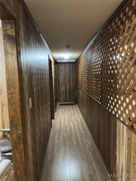 hall featuring wood walls, a textured ceiling, light wood-type flooring, and crown molding