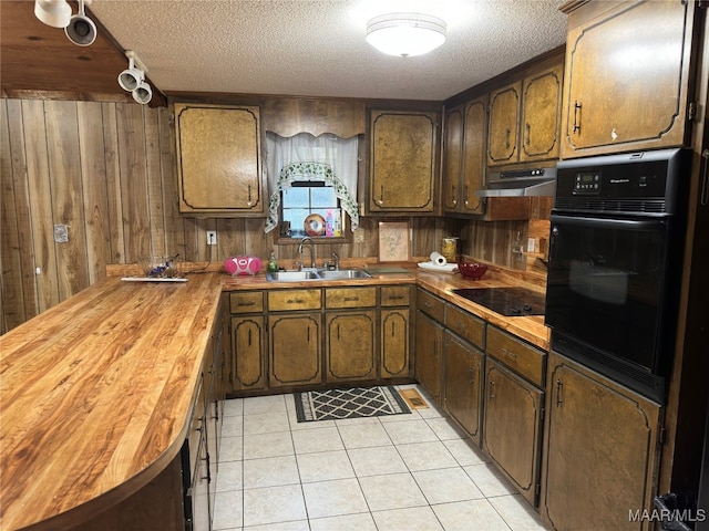 kitchen featuring black appliances, light tile patterned floors, wood counters, wooden walls, and sink