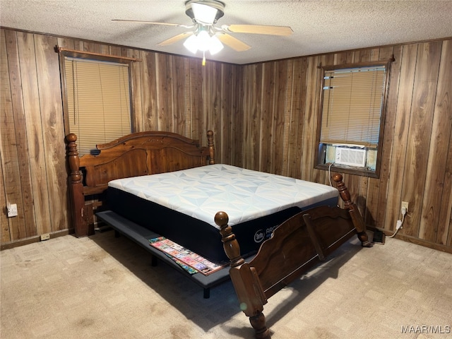 bedroom with cooling unit, a textured ceiling, wooden walls, light colored carpet, and ceiling fan