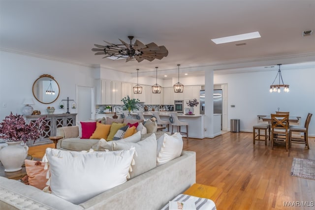 living room featuring light hardwood / wood-style floors, ceiling fan with notable chandelier, a skylight, and ornamental molding