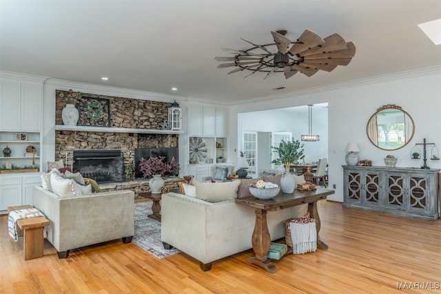 living room featuring ornamental molding, ceiling fan, a stone fireplace, and light hardwood / wood-style floors