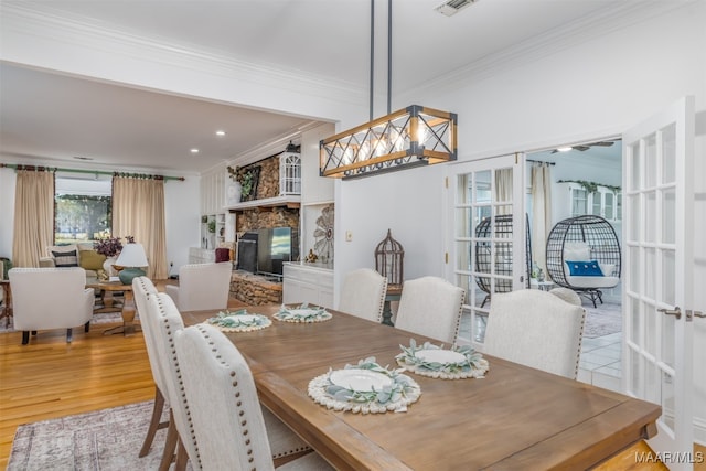 dining area featuring light hardwood / wood-style floors, a stone fireplace, and ornamental molding