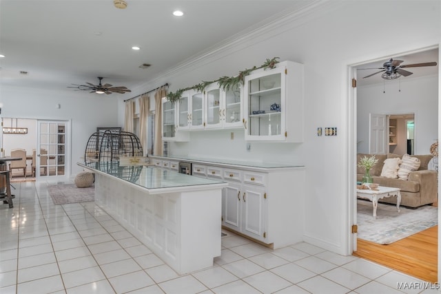 kitchen featuring light tile patterned flooring, a breakfast bar area, ceiling fan with notable chandelier, crown molding, and white cabinets