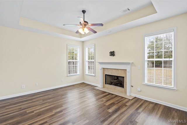 unfurnished living room with dark hardwood / wood-style flooring, a tiled fireplace, ceiling fan, and a raised ceiling