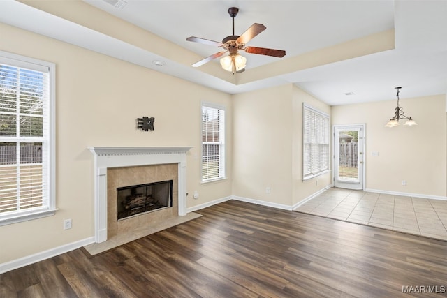 unfurnished living room featuring hardwood / wood-style floors, a tiled fireplace, plenty of natural light, and ceiling fan with notable chandelier