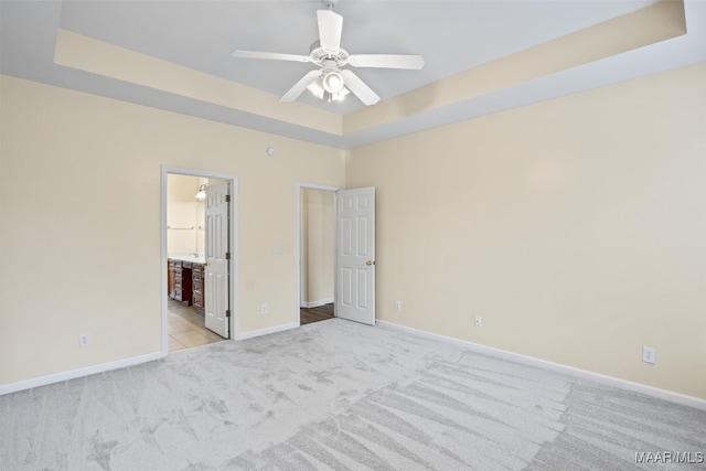 unfurnished bedroom with ensuite bath, light colored carpet, ceiling fan, and a raised ceiling