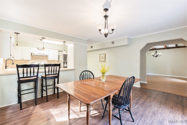 dining area with dark wood-type flooring, sink, an inviting chandelier, and crown molding