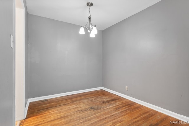 empty room with wood-type flooring and an inviting chandelier