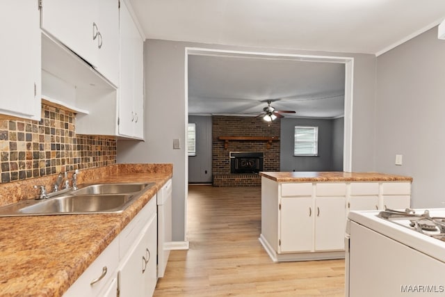 kitchen with white cabinets, sink, light hardwood / wood-style flooring, ceiling fan, and a fireplace