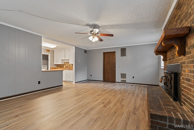 unfurnished living room with ornamental molding, a textured ceiling, ceiling fan, light hardwood / wood-style flooring, and a fireplace