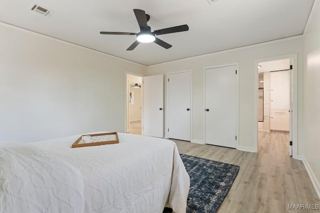 bedroom with two closets, crown molding, ceiling fan, and light wood-type flooring