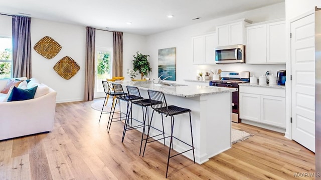 kitchen with a healthy amount of sunlight, a center island with sink, white cabinets, and appliances with stainless steel finishes