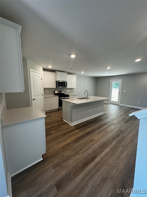 kitchen with sink, appliances with stainless steel finishes, white cabinetry, dark hardwood / wood-style floors, and a center island with sink