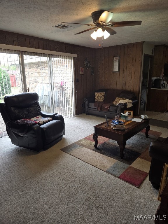 living room featuring wood walls, a textured ceiling, ceiling fan, and carpet floors