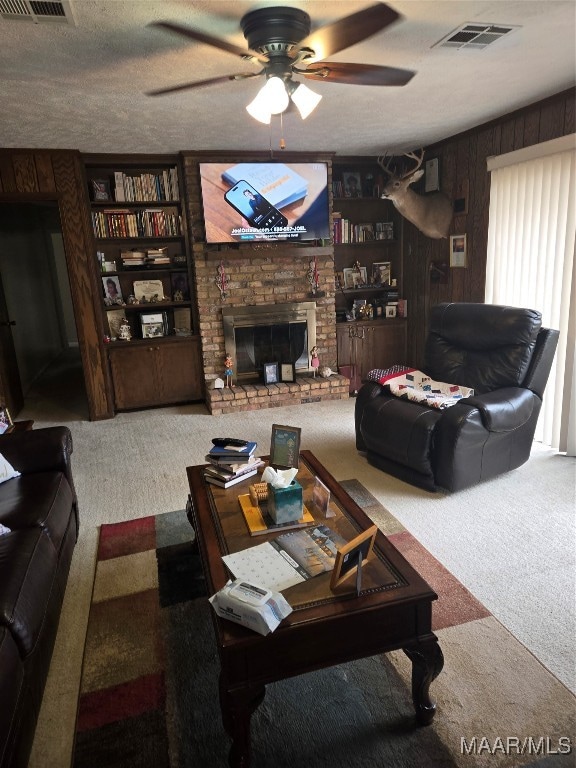 living room with a large fireplace, carpet floors, wooden walls, and ceiling fan