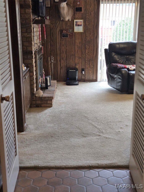 living room featuring a brick fireplace, wood walls, and carpet flooring