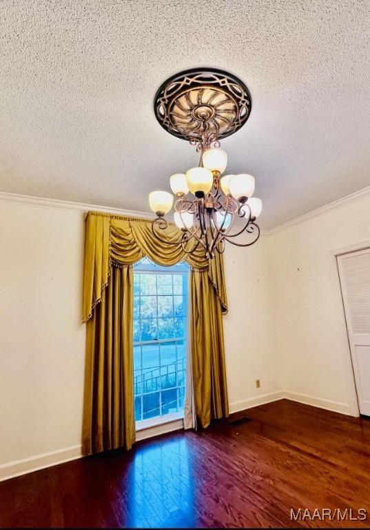 empty room featuring dark hardwood / wood-style flooring, a chandelier, a textured ceiling, and ornamental molding