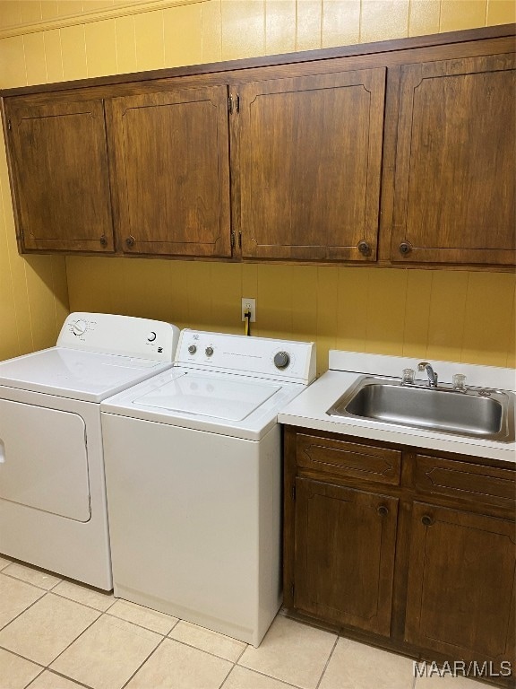 clothes washing area featuring washing machine and clothes dryer, sink, light tile patterned floors, and cabinets