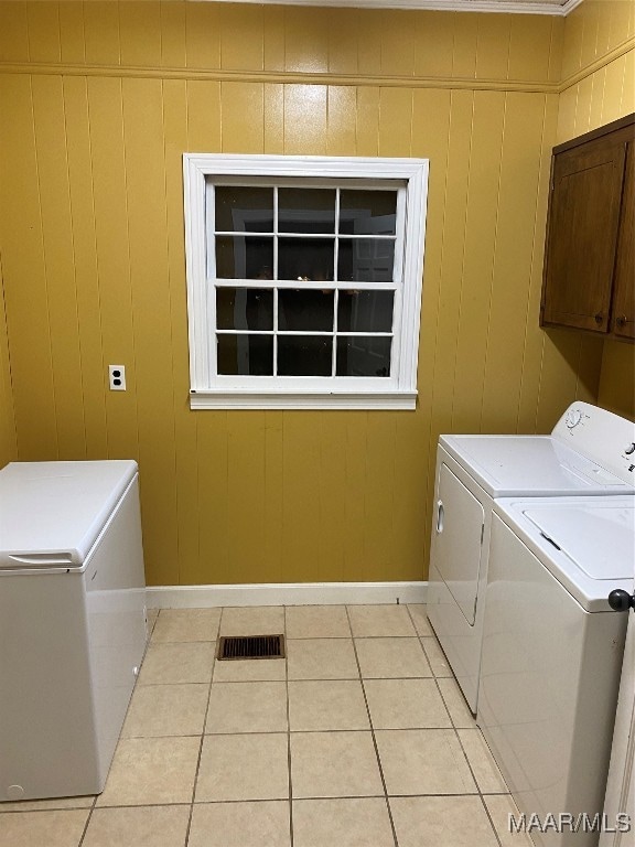 laundry room with cabinets, light tile patterned floors, wooden walls, and washing machine and clothes dryer