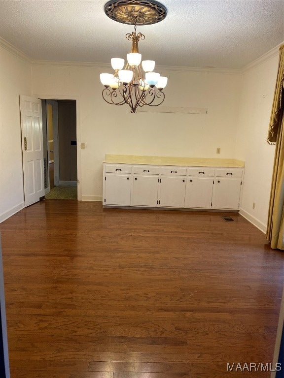 unfurnished dining area with dark hardwood / wood-style flooring, ornamental molding, a textured ceiling, and an inviting chandelier