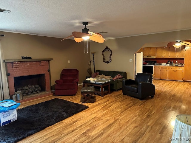 living room with a textured ceiling, ceiling fan, a fireplace, and light hardwood / wood-style flooring