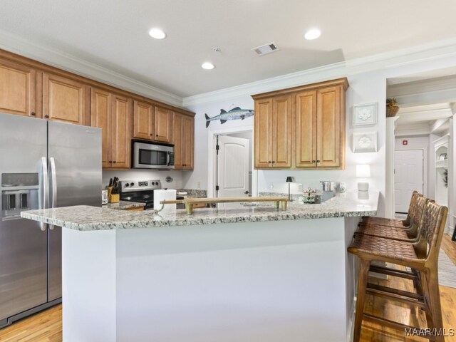 kitchen featuring stainless steel appliances, light hardwood / wood-style floors, light stone counters, a breakfast bar area, and crown molding