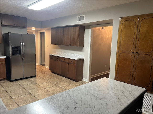 kitchen featuring stainless steel refrigerator with ice dispenser, a textured ceiling, and dark brown cabinets