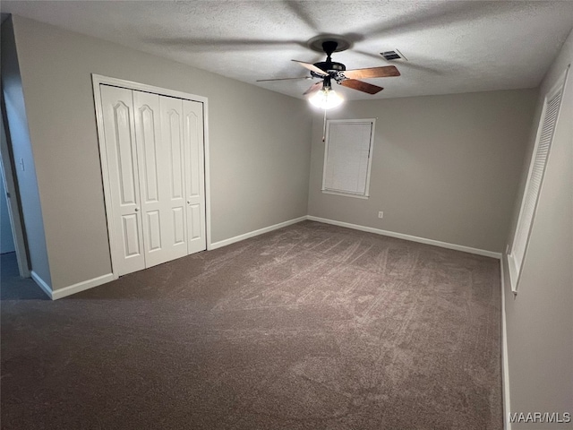 unfurnished bedroom with a closet, a textured ceiling, dark carpet, and ceiling fan