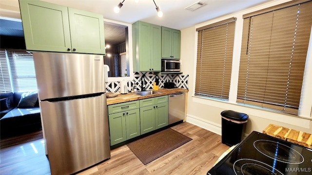 kitchen featuring green cabinets, decorative backsplash, stainless steel appliances, and butcher block countertops