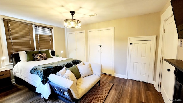 bedroom featuring dark hardwood / wood-style floors, two closets, and an inviting chandelier