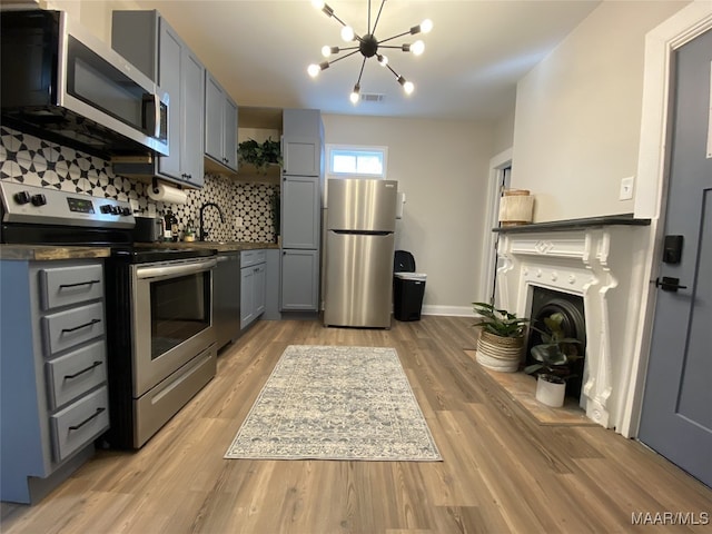 kitchen featuring light hardwood / wood-style floors, appliances with stainless steel finishes, a notable chandelier, gray cabinets, and decorative backsplash